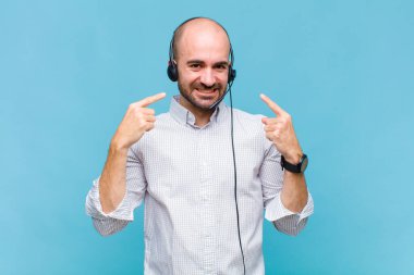 Kel adam kendine güvenerek gülümsüyor. Geniş gülüşünü gösteriyor. Olumlu, rahat, tatmin olmuş bir tavır.