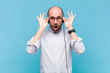 Kel adam şaşkın, şaşırmış ve şaşırmış hissediyor. Elinde şaşkın, inançsız bir bakışla gözlük tutuyor.