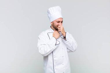 Kel bir adam boğazı ağrıyan ve grip belirtileri gösteren ağzı kapalı öksüren bir hasta.