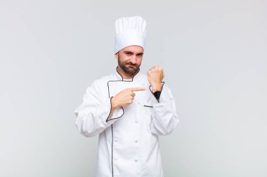 Kel adam sabırsız ve kızgın görünüyor, saati gösteriyor, dakiklik istiyor, zamanında gelmek istiyor.