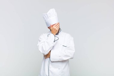 Kel bir adam stresli, utanmış ya da üzgün görünüyor, baş ağrısı var, yüzünü eliyle kapatıyor.