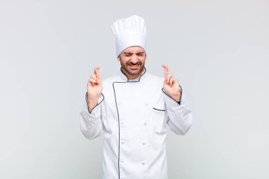 Kel adam gülümsüyor ve endişeyle iki parmağını çapraz yapıyor. Endişeli ve iyi şanslar diliyor.