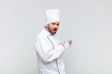 Kel adam şaşkın ve şaşırmış hissediyor. Kenardaki fotokopi alanını işaret ediyor. Şaşırmış, ağzı açık bir bakışla.