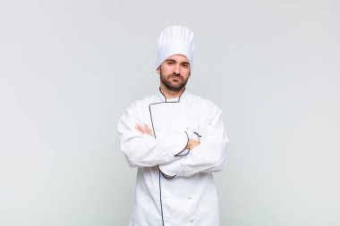 Kel adam mutsuz ve hayal kırıklığına uğramış, ciddi görünüyor, kızgın ve kollarını kavuşturmuş.