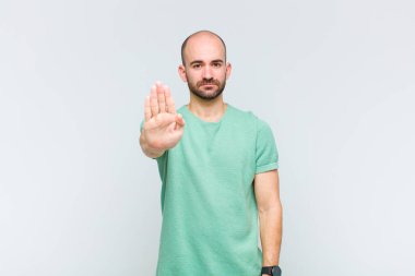 Kel adam ciddi, sert, hoşnutsuz ve kızgın görünüyor. Avuç içini açıp jesti durduruyor.