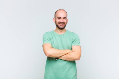 Kel adam mutlu, gururlu ve tatmin olmuş görünüyor. Kollarını kavuşturup gülümsüyor.