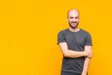 Kel adam utangaç ve neşeli bir şekilde gülüyor, arkadaş canlısı ve olumlu ama güvensiz bir tavırla.