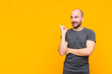 Kel adam mutlu bir şekilde gülümsüyor ve yan bakıyor, merak ediyor, düşünüyor ya da bir fikri var.