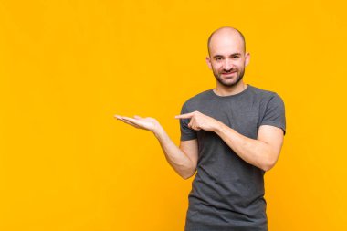 Kel adam gülümsüyor, mutlu, kaygısız ve tatmin olmuş hissediyor, fotokopi alanındaki konsepte veya fikre işaret ediyor.