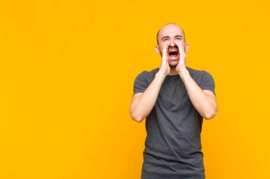 Kel adam mutlu, heyecanlı ve pozitif hissediyor. Elleri ağızda, bağırarak bağırıyor.