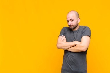 Kel adam omuz silkiyor, kafası karışık ve kararsız, kolları bağlı ve şaşkın bir şekilde şüpheye düşmüş görünüyor.