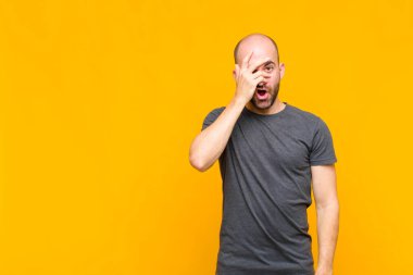 Kel adam şok olmuş, korkmuş ya da korkmuş görünüyor. Yüzü elle örtülmüş ve parmaklarının arasından gizlice bakıyor.