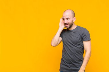 Kel adam gülümsüyor, tuhaf bir şekilde yan tarafa bakıyor, dedikoduları dinlemeye ya da bir sırrı duymaya çalışıyor.