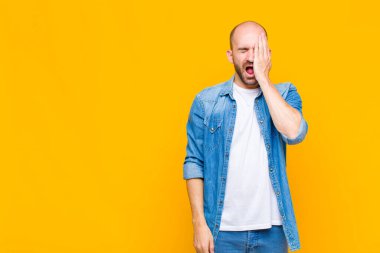 Kel adam uykulu görünüyor, sıkılmış ve esniyor, baş ağrısı ve yüzünün yarısını kaplayan bir eliyle