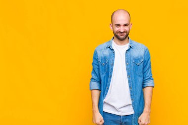 Kel adam pozitif ve kendinden emin gülümsüyor. Tatmin olmuş, arkadaş canlısı ve mutlu görünüyor.