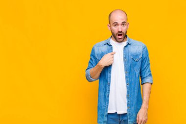 Şok olmuş ve ağzı açık, kendini işaret eden kel bir adam.