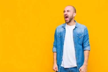 Kel adam öfkeyle bağırıyor, agresif bağırıyor, stresli ve sinirli görünüyor.