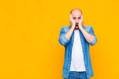 Kel adam mutsuz, korkmuş ya da endişeli görünüyor, ağzı sonuna kadar açık ve iki kulağını da elleriyle kapatıyor.