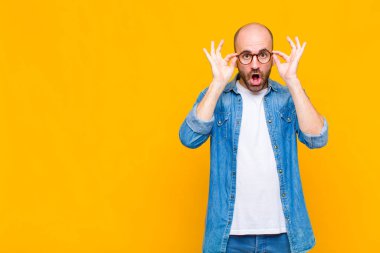 Kel adam şaşkın, şaşırmış ve şaşırmış hissediyor. Elinde şaşkın, inançsız bir bakışla gözlük tutuyor.