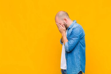 Kel adam üzgün, hayal kırıklığına uğramış bir bakışla gözlerini kapatıyor, ağlıyor, yan gözle bakıyor.