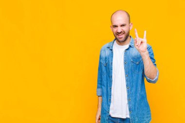 Kel adam mutlu, eğlenceli, kendinden emin, pozitif ve asi hissediyor, elle kaya veya heavy metal işareti yapıyor.