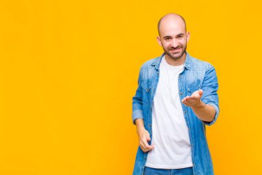 Kel adam gülümsüyor, mutlu görünüyor, kendinden emin ve arkadaş canlısı, anlaşma yapmak için el sıkışmayı teklif ediyor, işbirliği yapıyor.