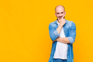 Kel adam ciddi görünüyor, düşünceli ve güvensiz, bir kolu çapraz ve çene üzerinde, seçenekleri tartıyor