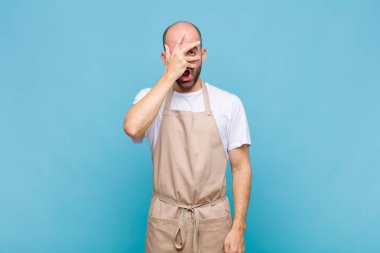 Kel adam şok olmuş, korkmuş ya da korkmuş görünüyor. Yüzü elle örtülmüş ve parmaklarının arasından gizlice bakıyor.