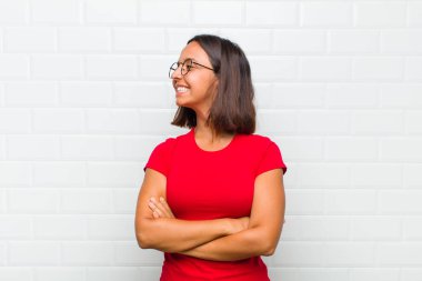 Latin kadın neşeyle gülümsüyor, mutlu, tatmin olmuş ve rahatlamış hissediyor, kollarını kavuşturup yan tarafa bakıyor.