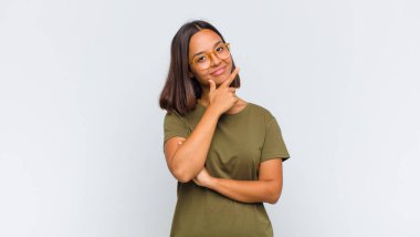 Latin bir kadın ciddi, düşünceli ve güvensiz görünüyor. Bir kolu çapraz, eli çenesinde, seçenekleri değerlendiriyor.