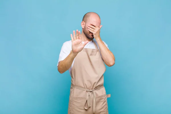 bald man covering face with hand and putting other hand up front to stop camera, refusing photos or pictures