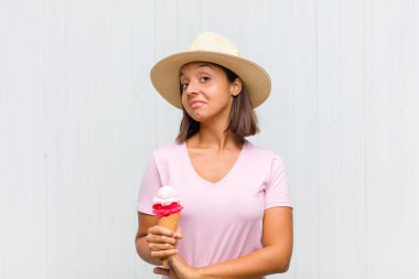 Genç İspanyol kadın omuz silkiyor, kafası karışık ve emin değil, kolları bağlı ve şaşkın görünüyor.