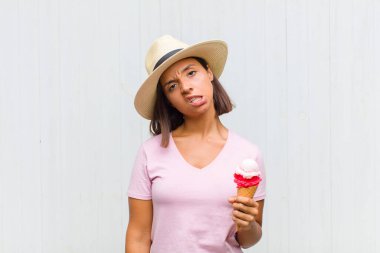 young hispanic woman feeling puzzled and confused, with a dumb, stunned expression looking at something unexpected