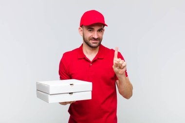 Genç kel adam gülümsüyor ve arkadaş canlısı görünüyor. Bir numarayı gösteriyor ya da ilk eli önde, geri sayıyor.