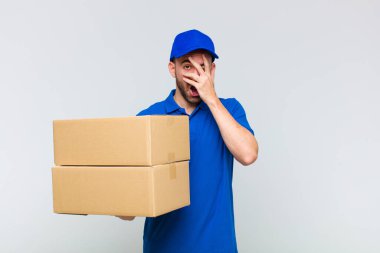 Genç kel adam şok olmuş, korkmuş ya da korkmuş görünüyor. Yüzü elle kaplanmış ve parmaklarının arasından gizlice bakıyor.