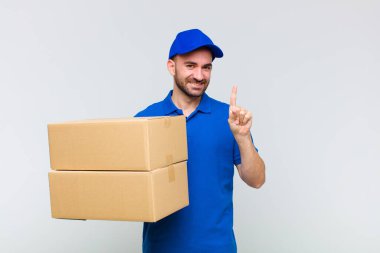 Genç kel adam gülümsüyor ve arkadaş canlısı görünüyor. Bir numarayı gösteriyor ya da ilk eli önde, geri sayıyor.