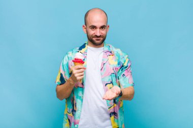 Genç kel adam mutlu bir şekilde gülümsüyor, arkadaş canlısı, kendinden emin, pozitif bakışlı, bir nesne ya da konsept sunuyor ve gösteriyor.