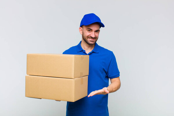 young bald man smiling cheerfully, feeling happy and showing a concept in copy space with palm of hand