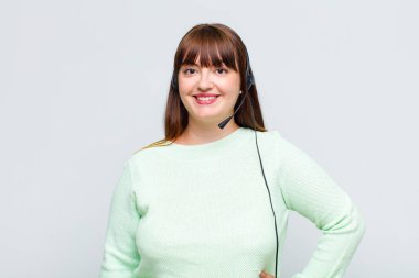 Ayrıca eli kalçasında, kendinden emin, olumlu, gururlu ve arkadaş canlısı bir şekilde gülümseyen cüsseli bir kadın.