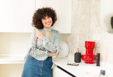 Genç, güzel bir kadın neşeli bir şekilde gülümsüyor, mutlu hissediyor ve kenarı ve yukarıyı işaret ediyor, kopyalama alanında nesneler gösteriyor.