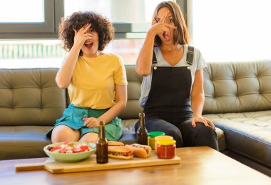 Genç, güzel bir kadın şok olmuş, korkmuş ya da korkmuş görünüyor. Yüzü elle kaplanmış ve parmaklarının arasından gizlice bakıyor.