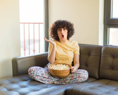 Genç ve güzel bir kadın şaşırmış ve şok olmuş görünüyor, çenesi düşmüş, bir objeyi elinde açık bir elle tutuyor.