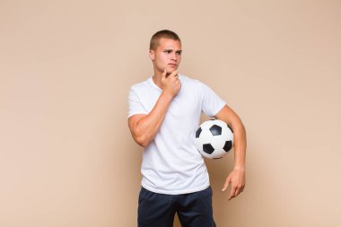 Genç sarışın adam mutlu, kendinden emin bir ifadeyle gülümsüyor. Elleri çenesinde, merak ediyor ve yan tarafa bakıyor.