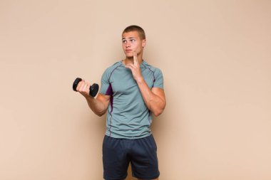 Genç sarışın adam mutlu bir şekilde gülümsüyor ve hayal kuruyor ya da şüphe ediyor, yan tarafa bakıyor.