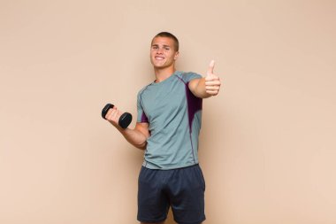 Genç sarışın adam gururlu, tasasız, kendinden emin ve mutlu, başparmağıyla olumlu gülümsüyor.