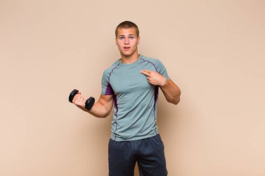 Genç sarışın adam şok olmuş ve şaşırmış görünüyor ağzı açık, kendini işaret ediyor.