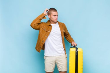 Genç sarışın adam şaşkın ve şaşkın hissediyor, başını kaşıyor ve yan tarafa bakıyor.