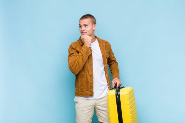 Genç sarışın adam mutlu, kendinden emin bir ifadeyle gülümsüyor. Elleri çenesinde, merak ediyor ve yan tarafa bakıyor.