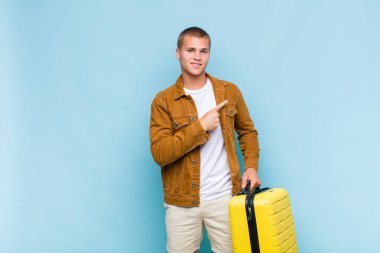 Genç sarışın adam neşeyle gülümsüyor, mutlu hissediyor ve kenarı ve yukarıyı işaret ediyor, fotokopi uzayındaki nesneleri gösteriyor.
