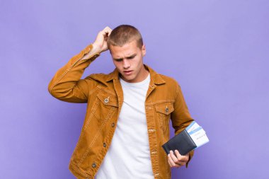 Genç sarışın adam şaşkın ve şaşkın hissediyor, başını kaşıyor ve yan tarafa bakıyor.